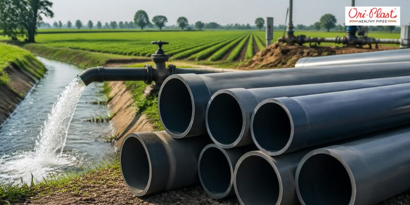 A large stack of heat resistant PVC pipes discharging water into an irrigation canal on a farm.