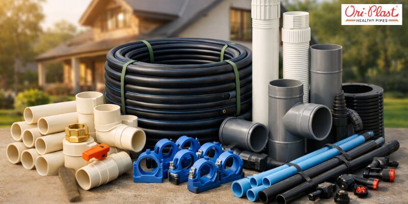 A variety of premium Ori-Plast PVC, CPVC pipes, large black hose coils, and blue pipe clamps arranged neatly outdoors in front of a modern residential building.