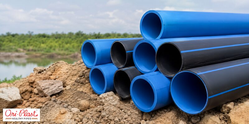 Durable blue and black casing pipes stacked on muddy soil at a regional rural water supply project site.