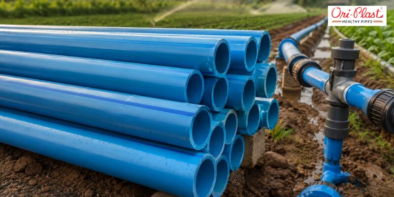 Stacked blue agricultural pipes with blue stripe PVC pipe marking laid out near an active farm field irrigation setup.